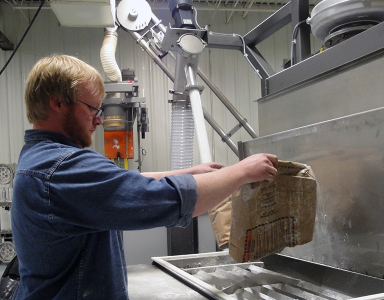 Operator breaking and emptying a bag of material into a bag dump station