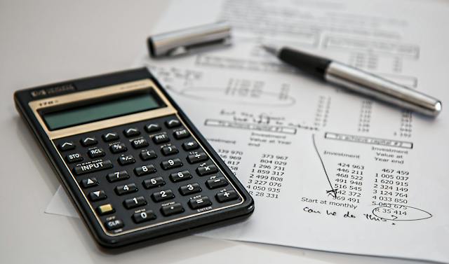 A black calculator, pen, and white printed paper